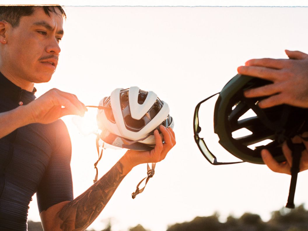 Two riders hold their helmets at golden hour.